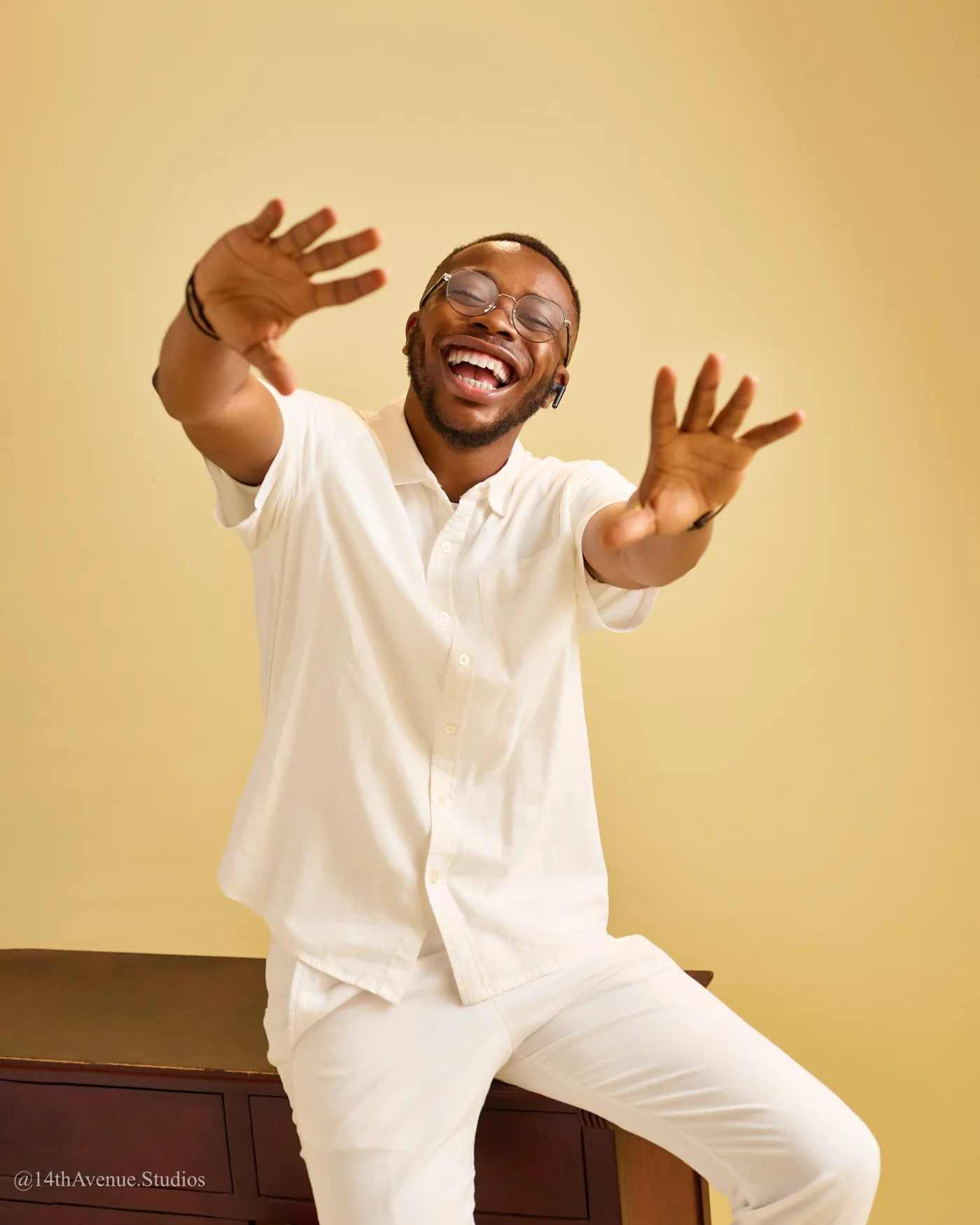 Gideon Agbeniga in white, laughing with both hands stretched towards the camera